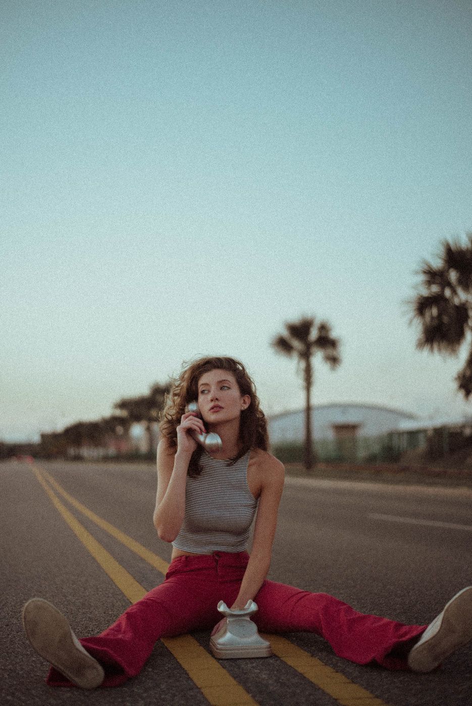 A portrait of a girl holding a telephone sitting in the middle of the road.