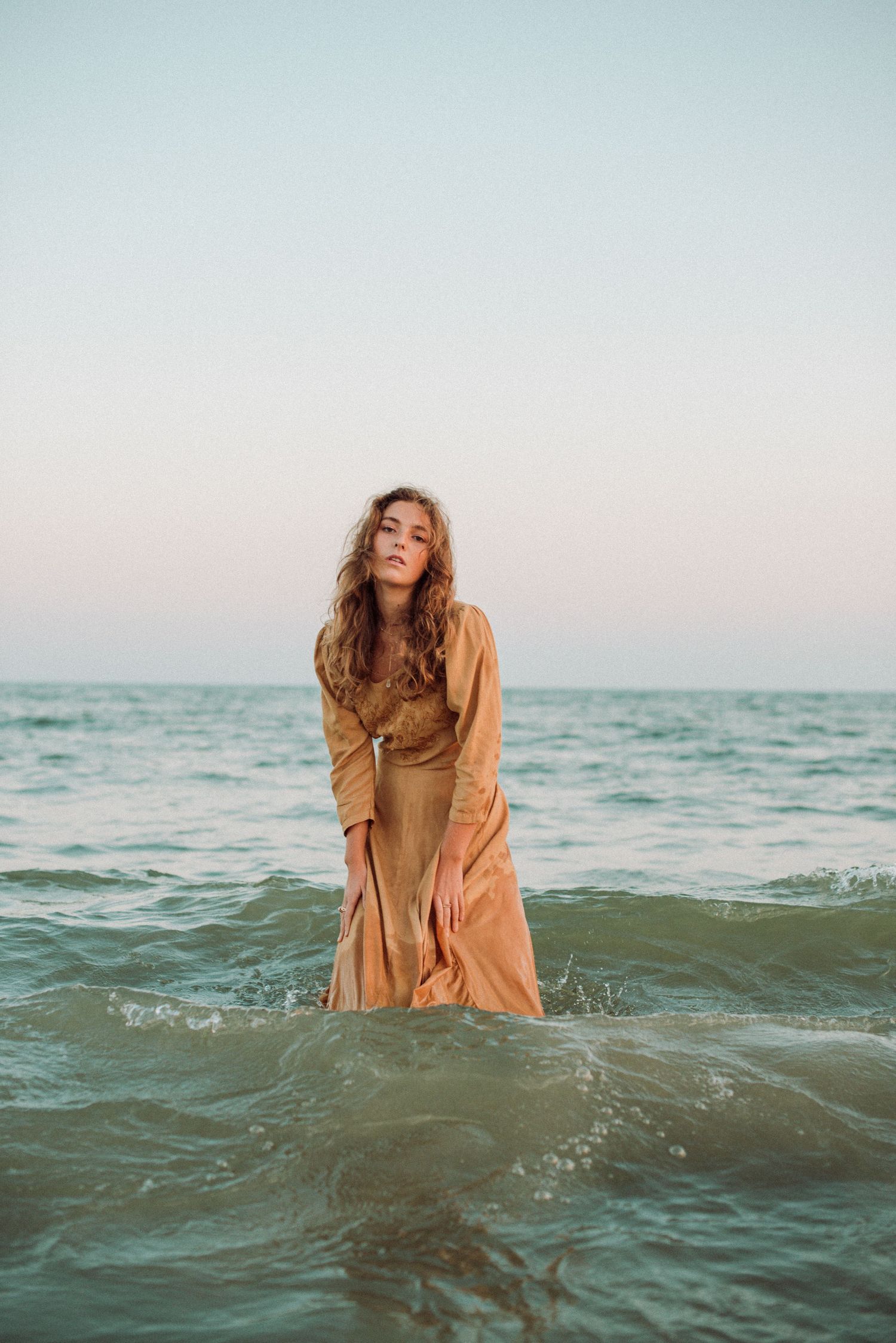A portrait of a girl posing and standing in the ocean water with a dress on.