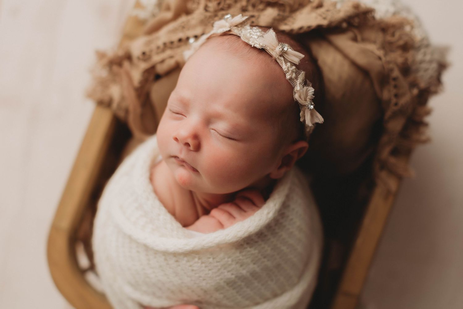 Peaceful newborn baby swaddled in green wrap sleeping in wooden bowl with white fur padding. Philadelphia newborn Photographer.