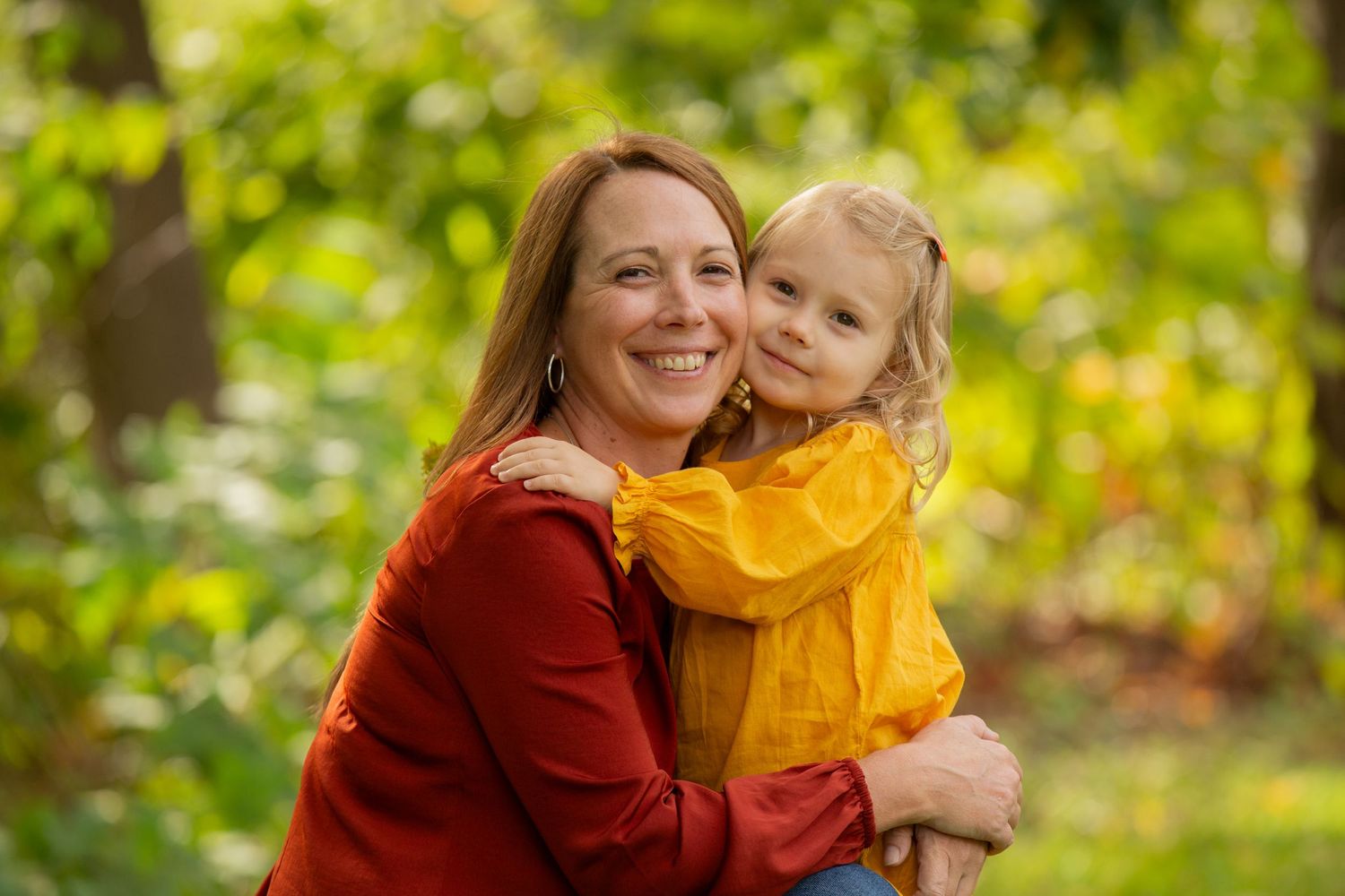 Parent and child sharing a joyful moment outdoors with bright green foliage in the background.