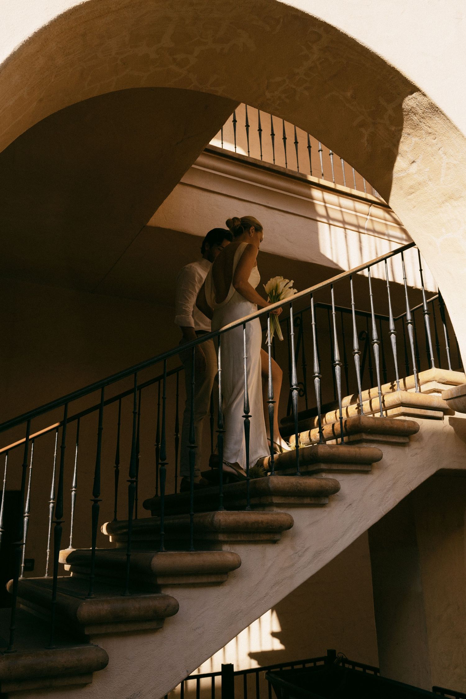 A couple embracing on a curved staircase under an arched ceiling.