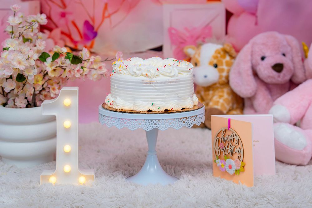 Simple white birthday cake displayed on blue pedestal with illuminated number one sign.