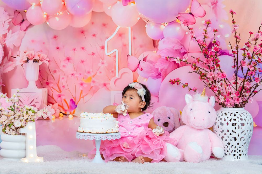 Elegant first birthday scene with white cake, pink balloons, and cherry blossom decorations.