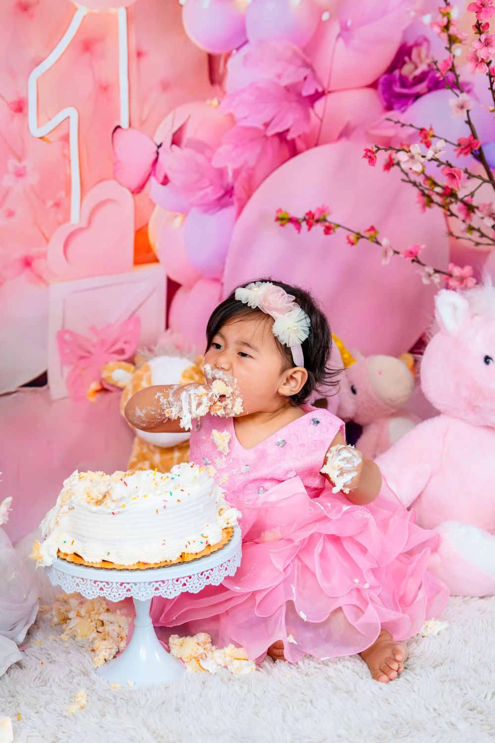 First birthday celebration with baby eating cake surrounded by pink decorations.