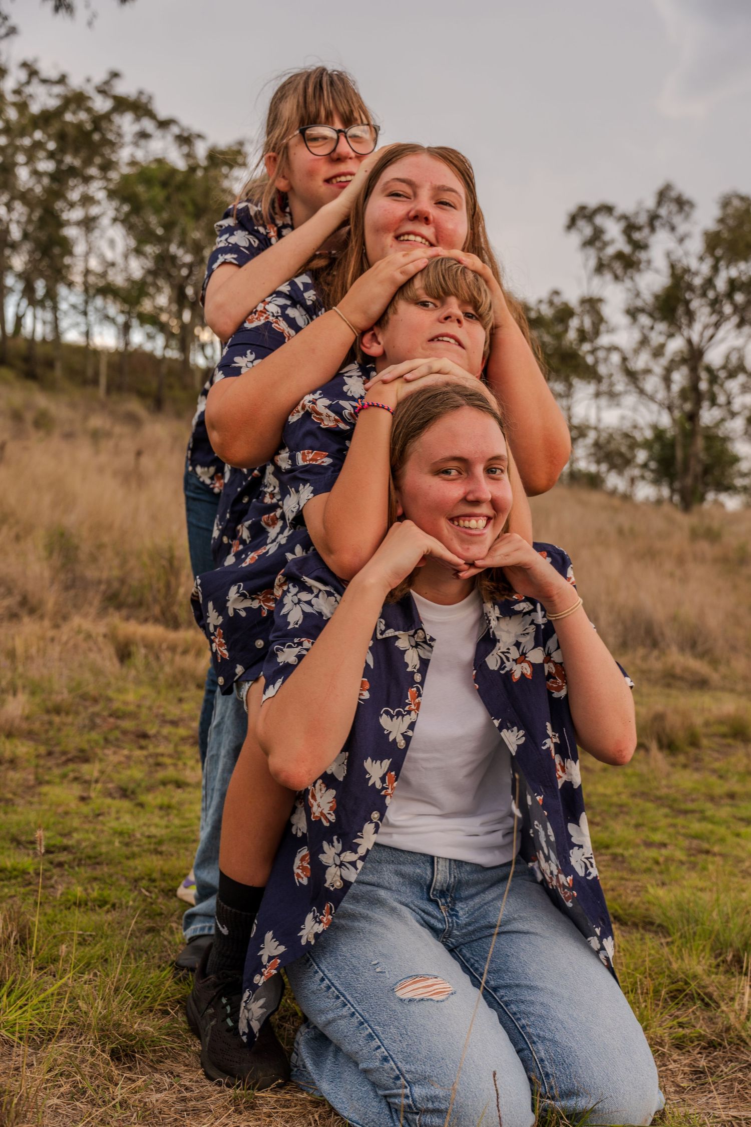Friends stack in a cheerful pose wearing coordinated floral outfits on a grassy hillside.