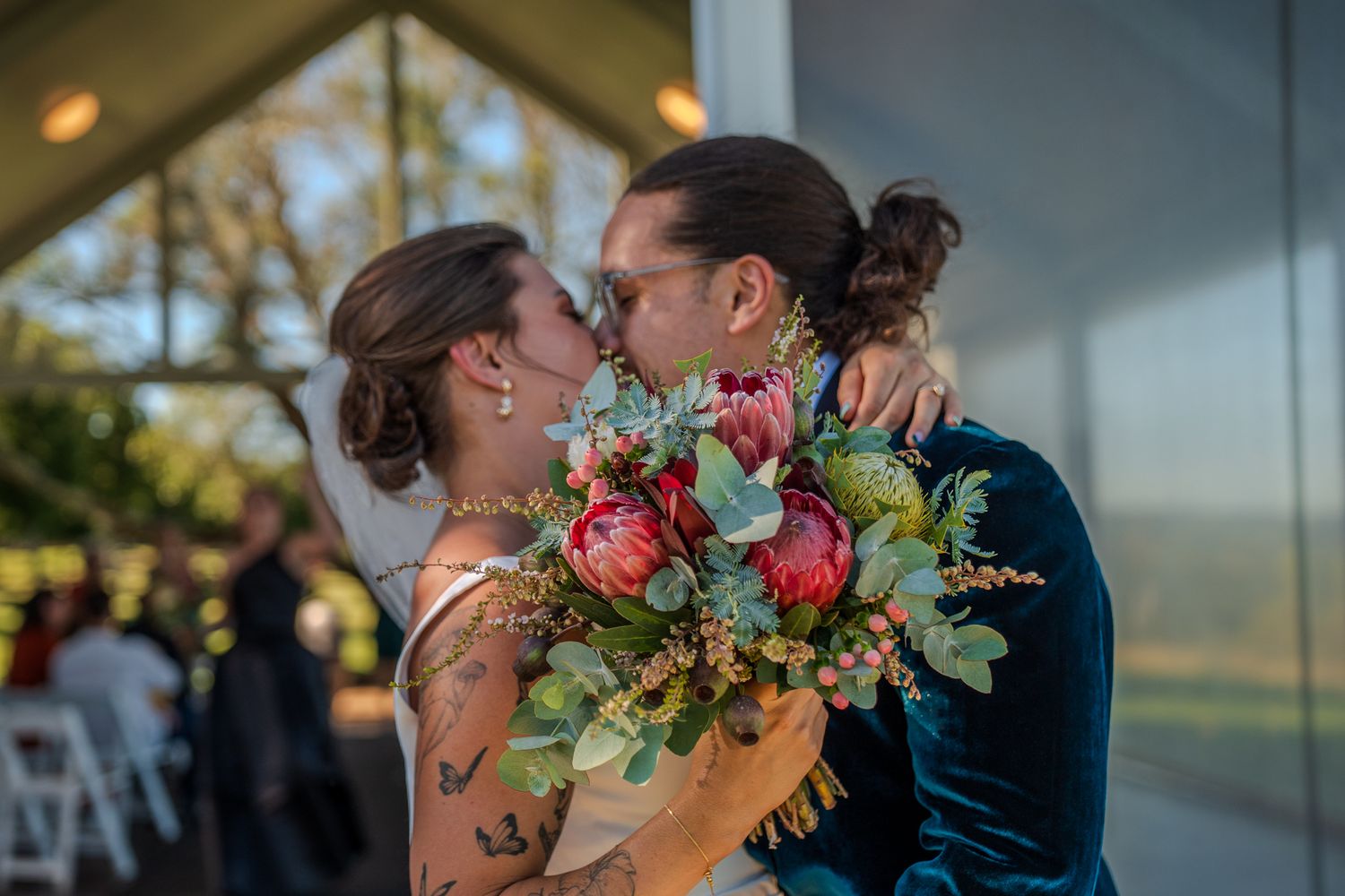 Couple shares an intimate moment with a vibrant bouquet of flowers at an outdoor wedding venue.