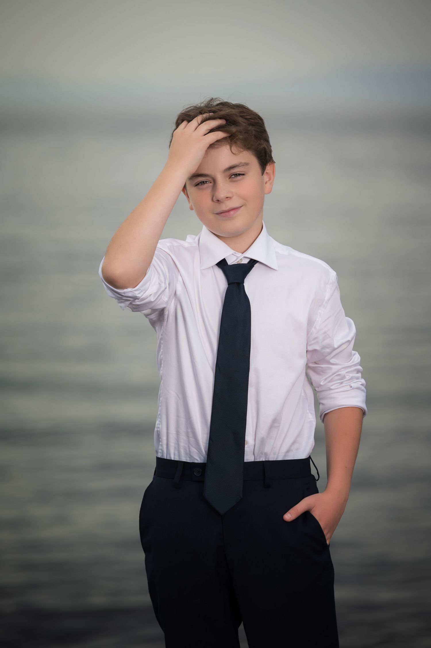 Young person in formal attire posing against grey background in casual poses.