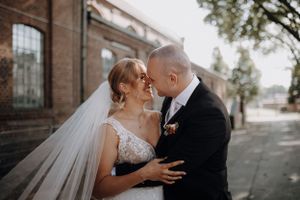 Bride and groom sharing intimate moment, nearly kissing outside historic brick building.