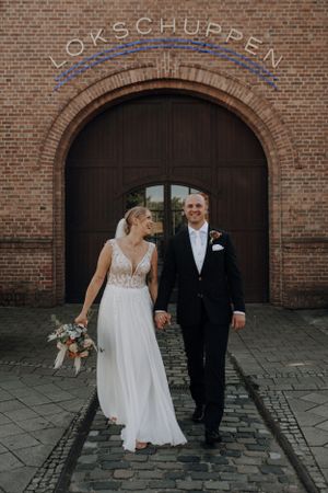 Happy bride and groom walking hand in hand before Lokschuppen brick arch entrance.