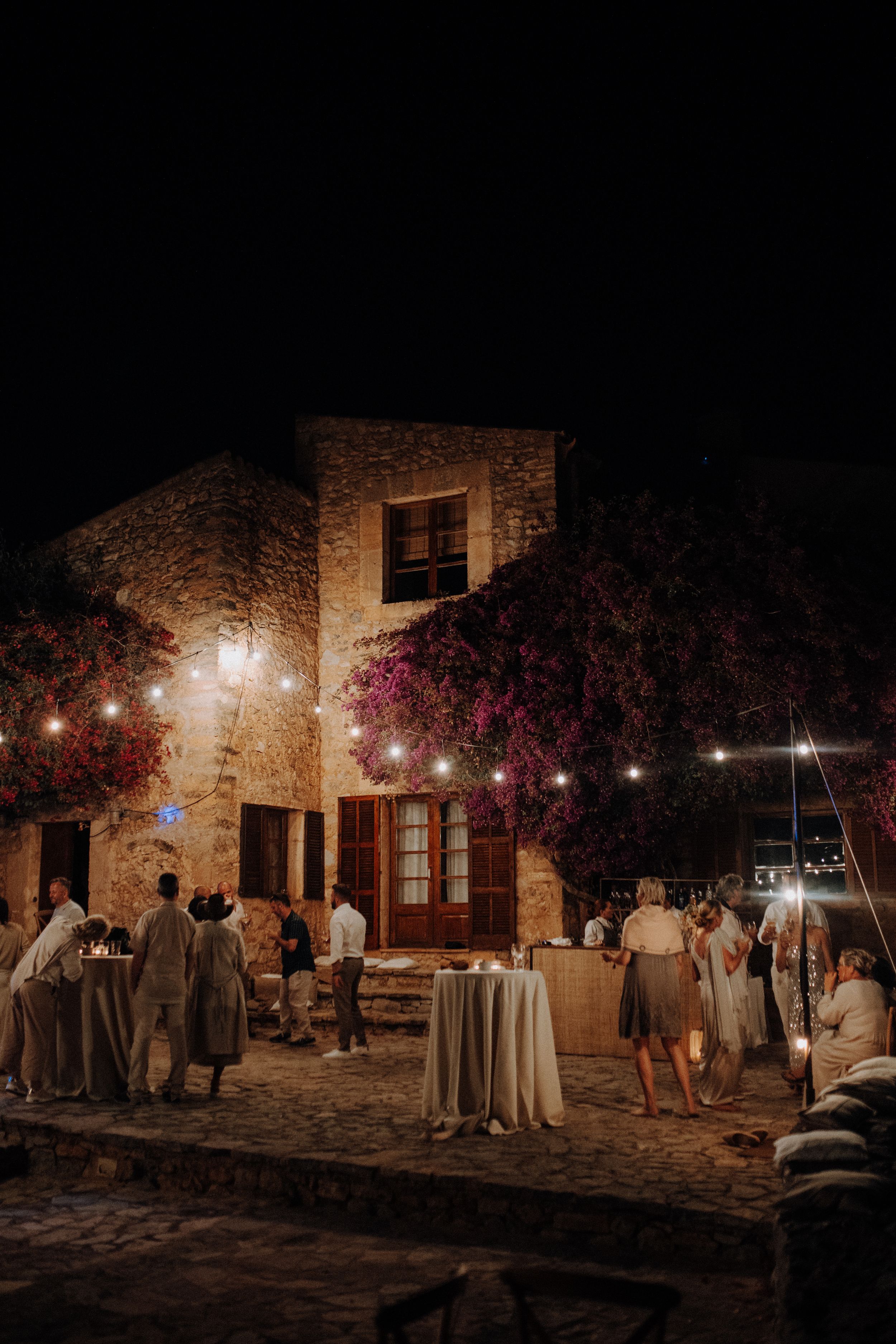 Guests mingling outside a rustic stone venue decorated with fairy lights at night.