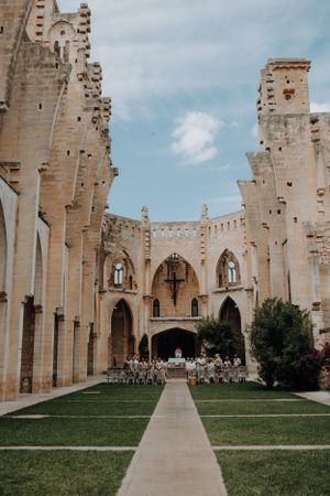 Outdoor wedding ceremony set in stunning Gothic stone ruins with guests seated on green lawn.
