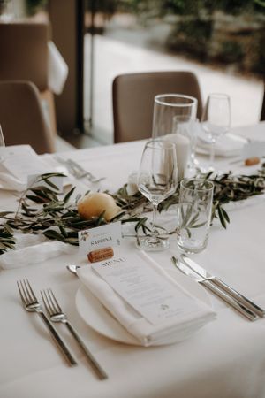 Elegant wedding table setting with olive branch garland, wine glasses, and personalized menu card.