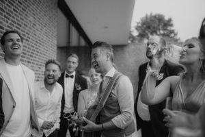 Black and white photo of groom and guests laughing at outdoor wedding reception.
