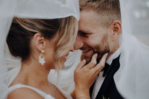 Close-up of smiling bride and groom touching foreheads under wedding veil.