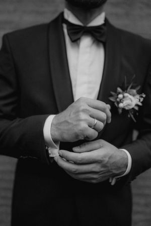 Black and white close-up of groom in tuxedo adjusting cufflinks with boutonniere.