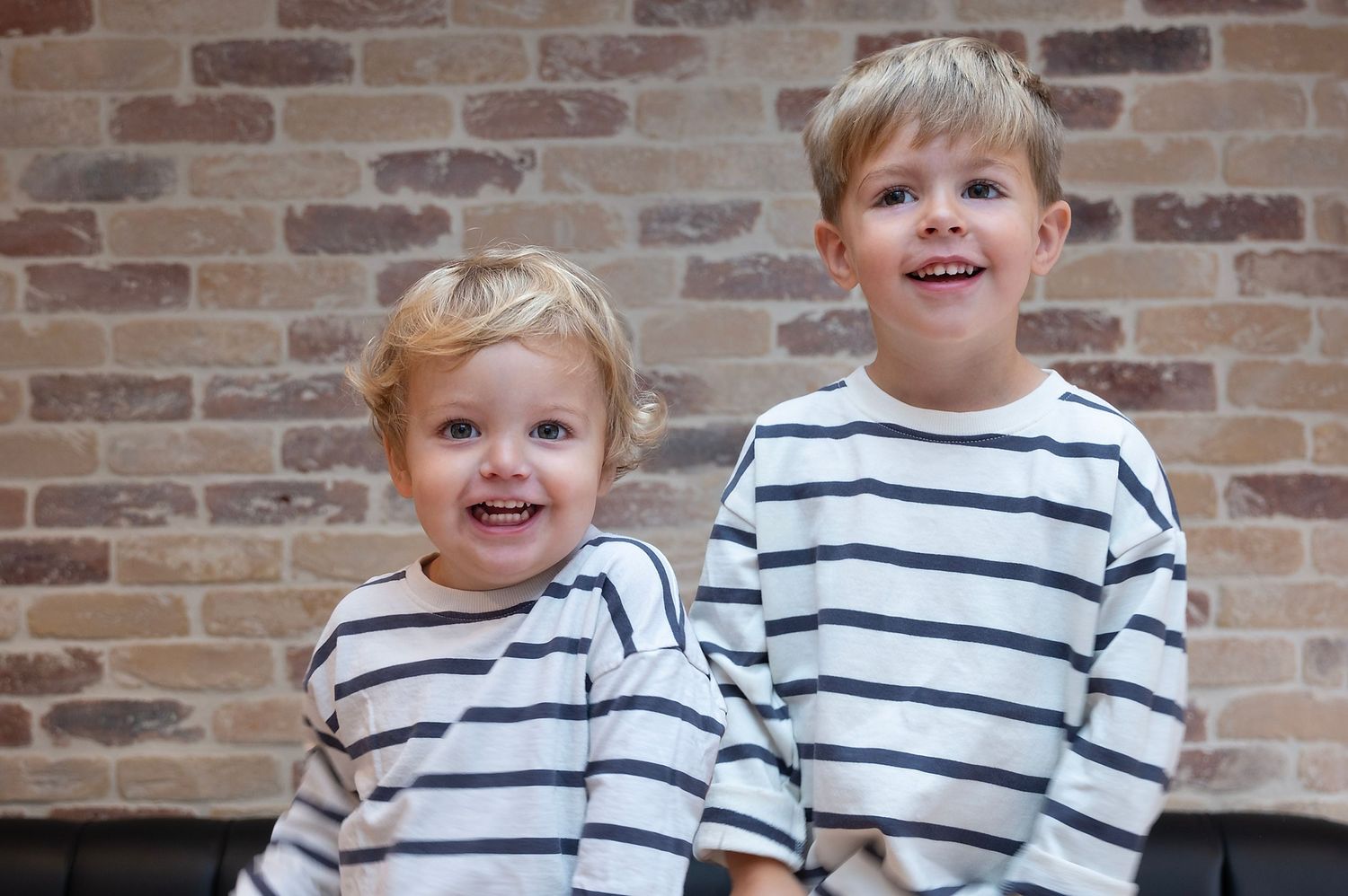 two brothers smiling at the camera with a brick background