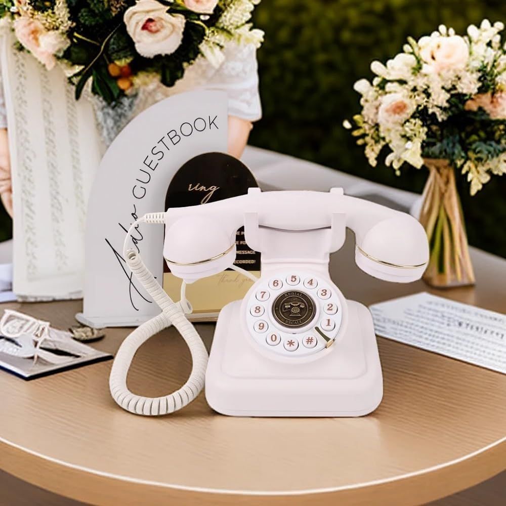 Vintage white rotary telephone on table with floral arrangements at wedding guest book station.