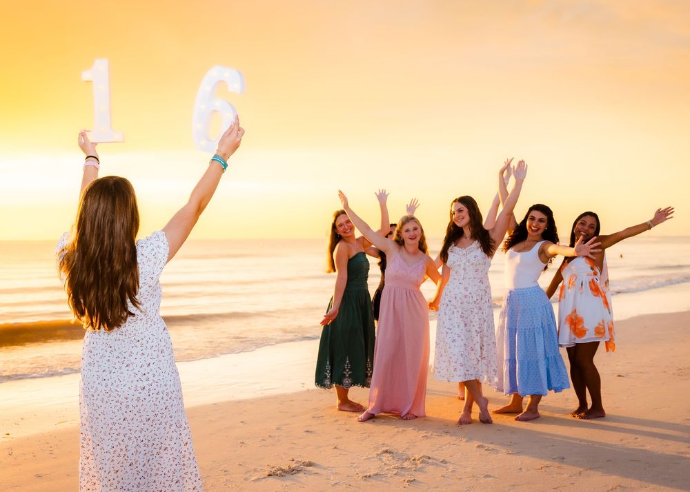 Girls celebrating a Sweet 16 birthday on the beach at golden sunset, one holding large number balloons.
