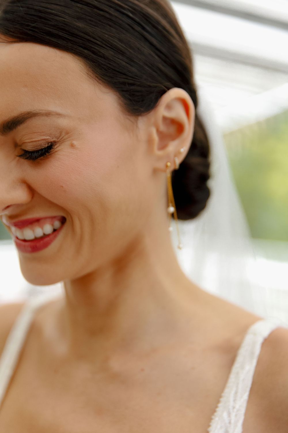 Detail shot of smiling bride wearing delicate drop earrings and natural makeup.