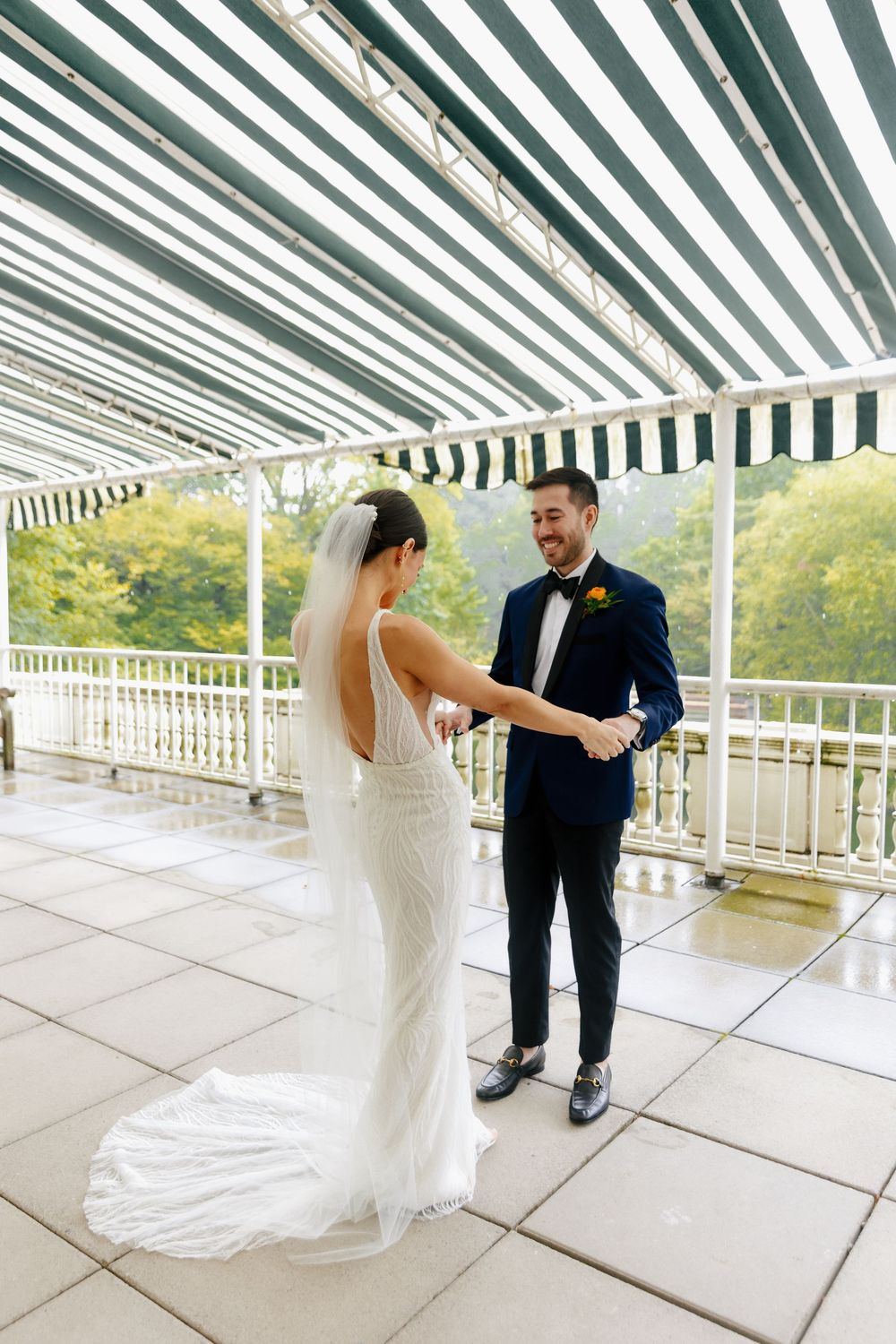 Wedding couple sharing first look moment under striped awning on outdoor terrace.