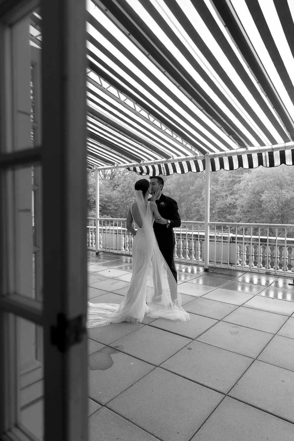Black and white series of wedding couple's first look on covered terrace with striped canopy.