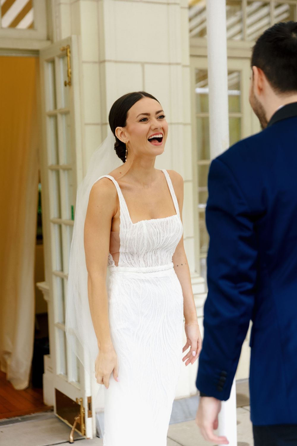 Bride in white dress smiling during first look moment with groom.