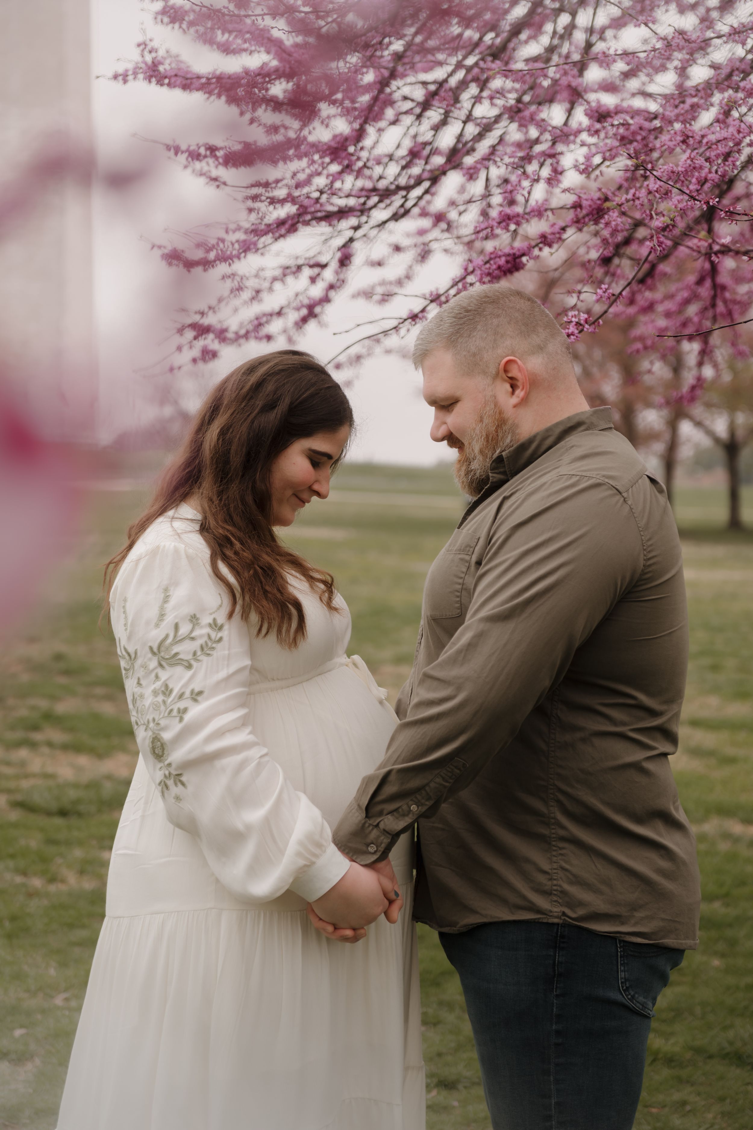 Couple embraces under blooming cherry blossoms with the Washington Monument in background during spring.