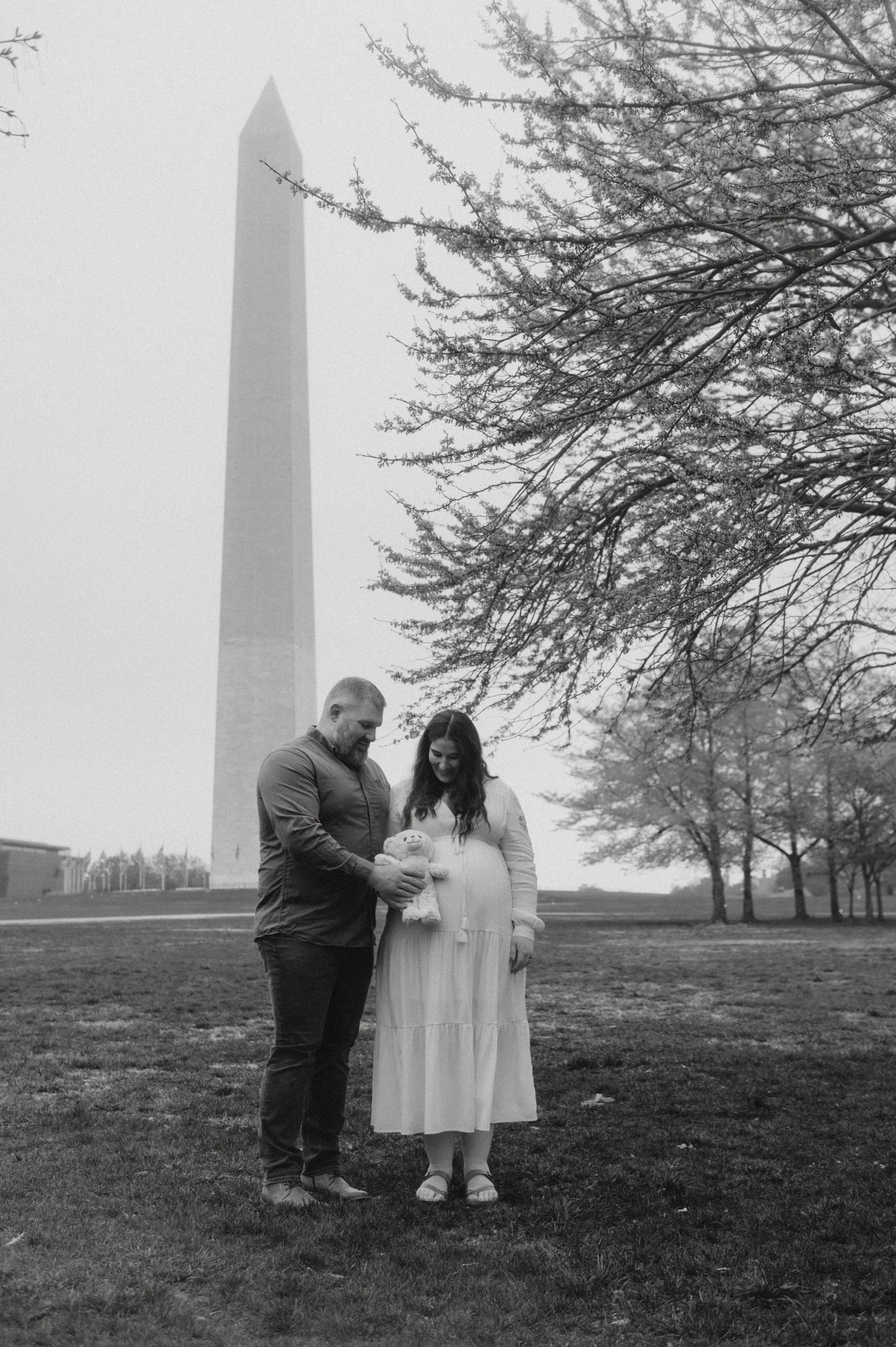 A couple stands together on the National Mall with the Washington Monument rising in the misty background.