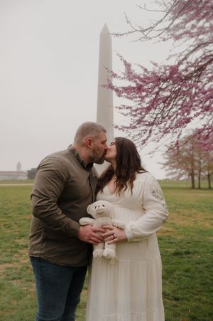 Romantic maternity photo shoot with couple holding stuffed animal under cherry blossoms by Washington Monument.