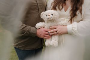 Couple in casual attire holding a white teddy bear together in a dreamy outdoor setting.