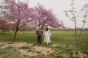 A couple walks together under blooming cherry blossom trees in a spring garden setting.