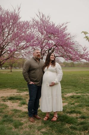 A couple stands beneath a beautiful blooming cherry blossom tree in a spring park setting.