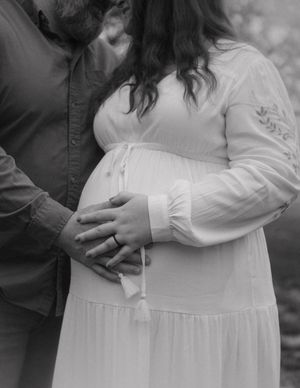 Black and white close up of couple tenderly holding pregnant belly in flowing white maternity dress.