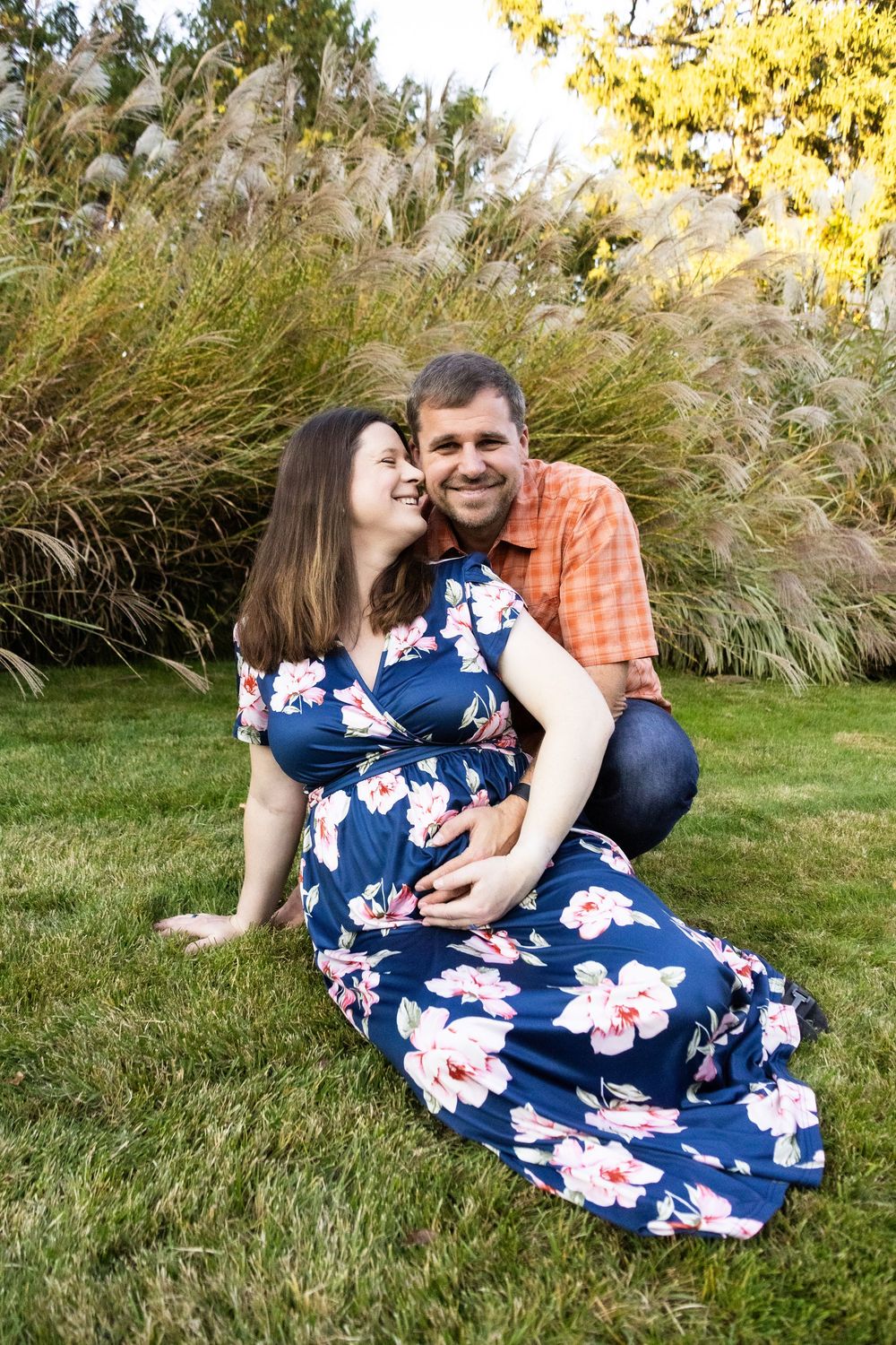 Couple relaxing on grass in autumn setting with ornamental grasses and golden light.