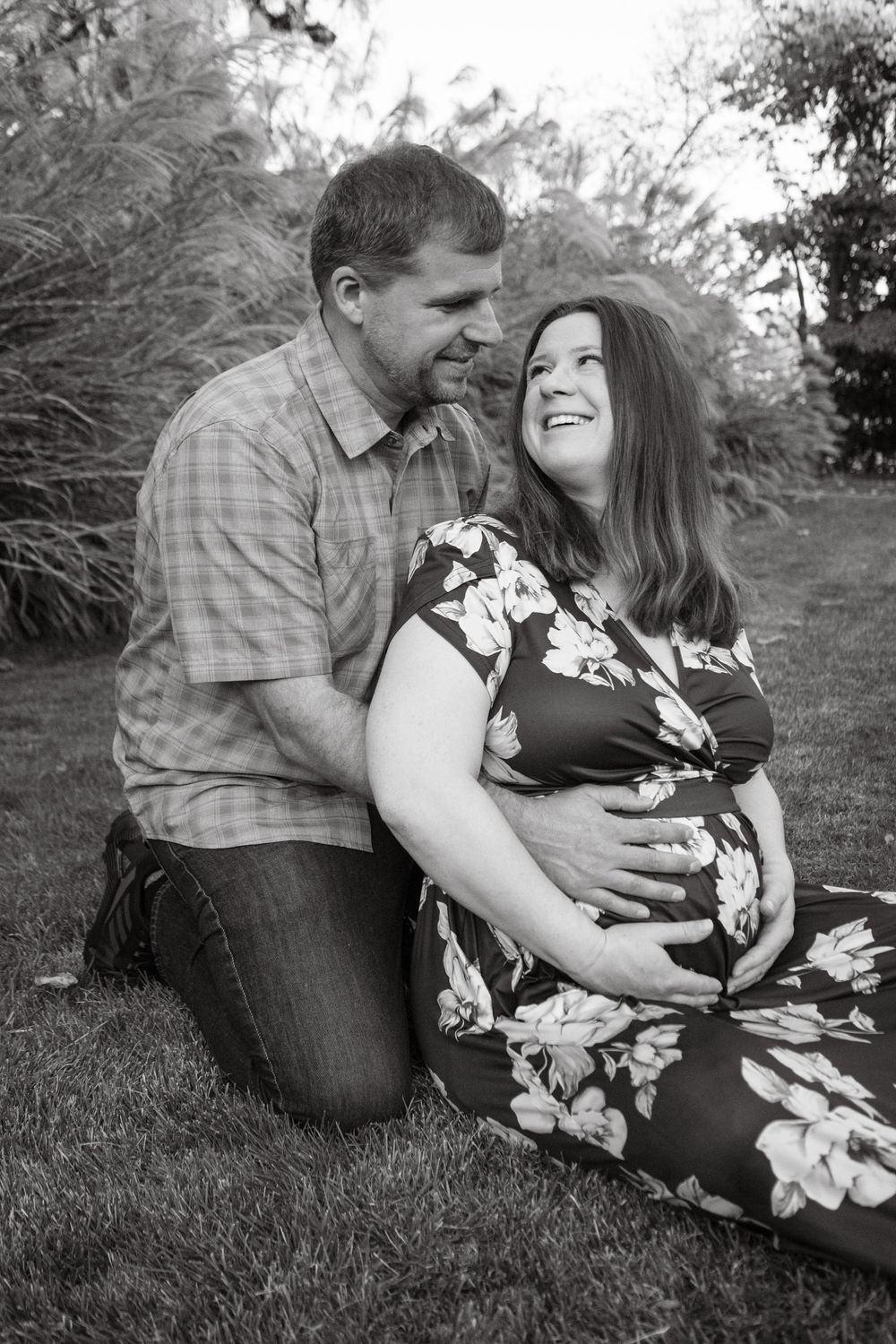 Romantic couple in casual attire sharing intimate moments while sitting on grass in a natural outdoor setting.