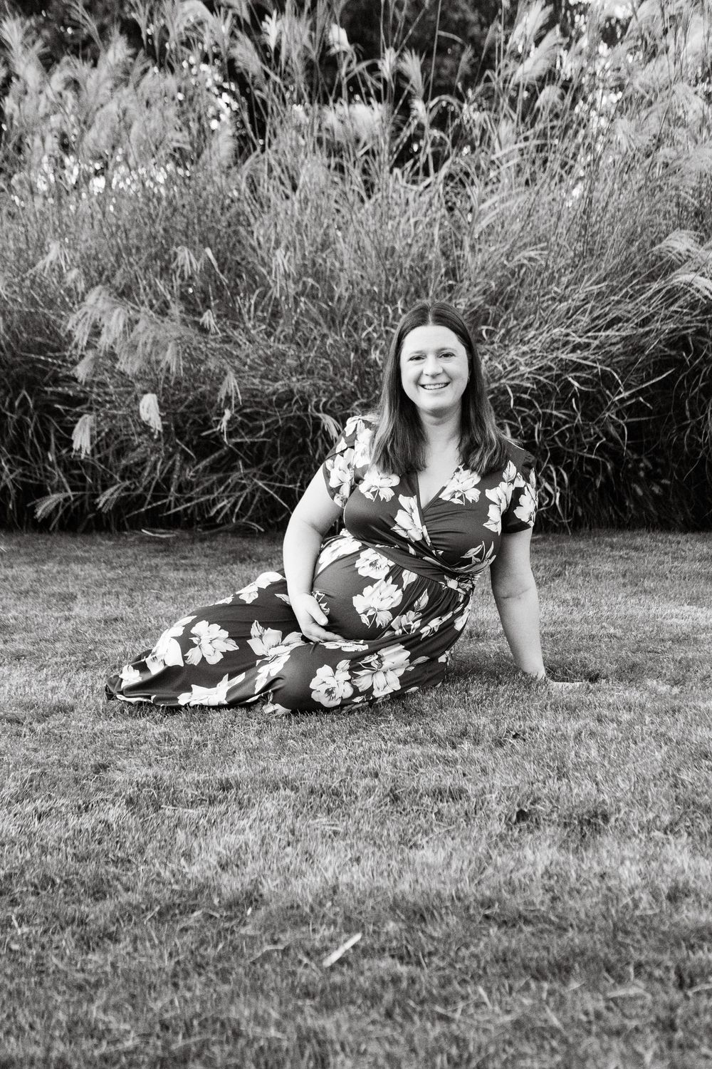 Woman in floral dress lying on grass smiling and relaxing in an outdoor garden setting.