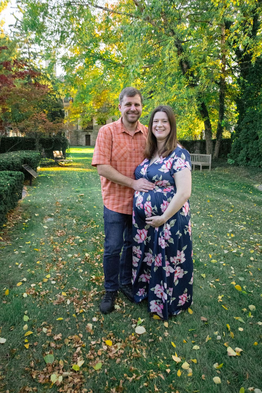 Couple posing together on lawn with fall foliage and trees in background.