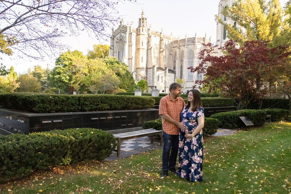 A couple poses in front of a gothic cathedral surrounded by autumn foliage and manicured gardens.