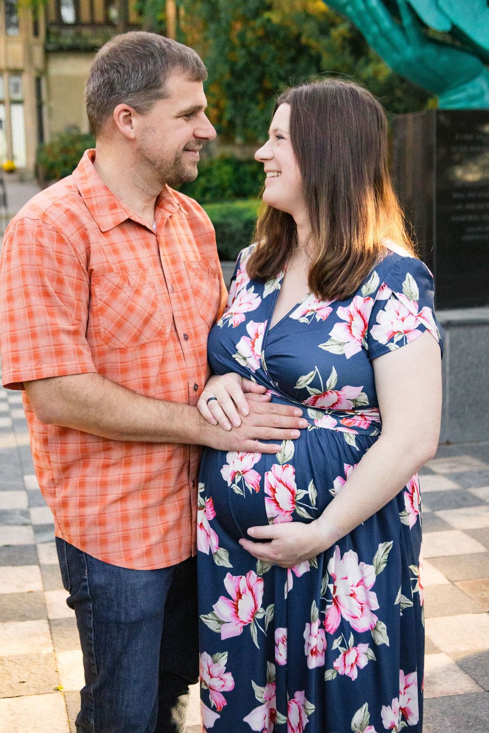 Couple in coordinating orange and navy outfits embrace during outdoor maternity photoshoot.