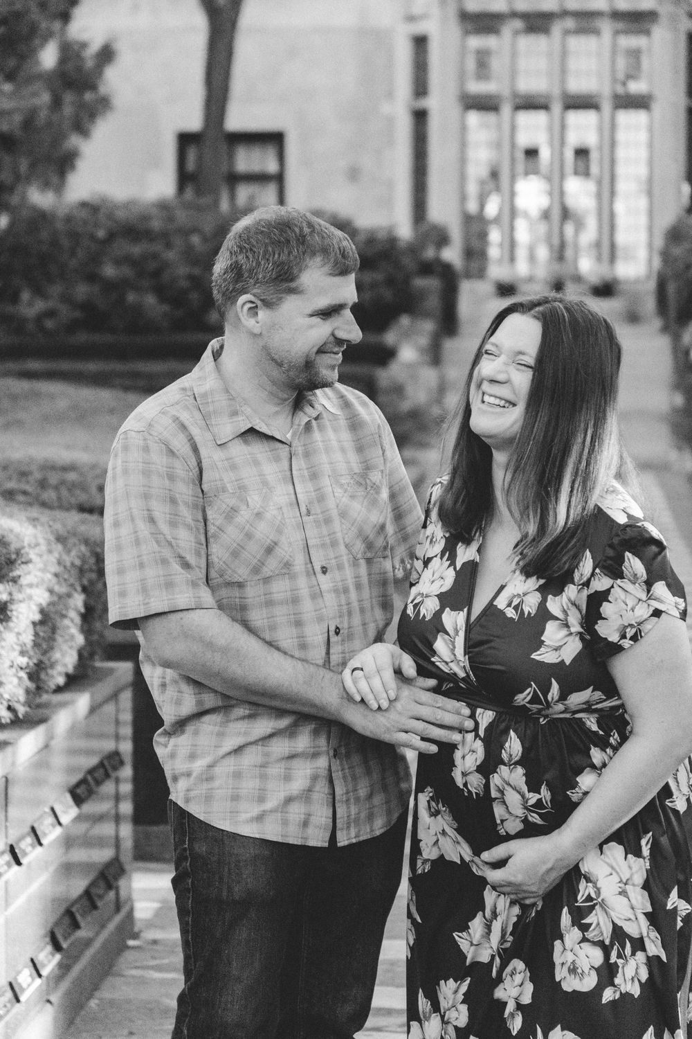 A couple shares a candid laughing moment together outdoors in black and white photography.