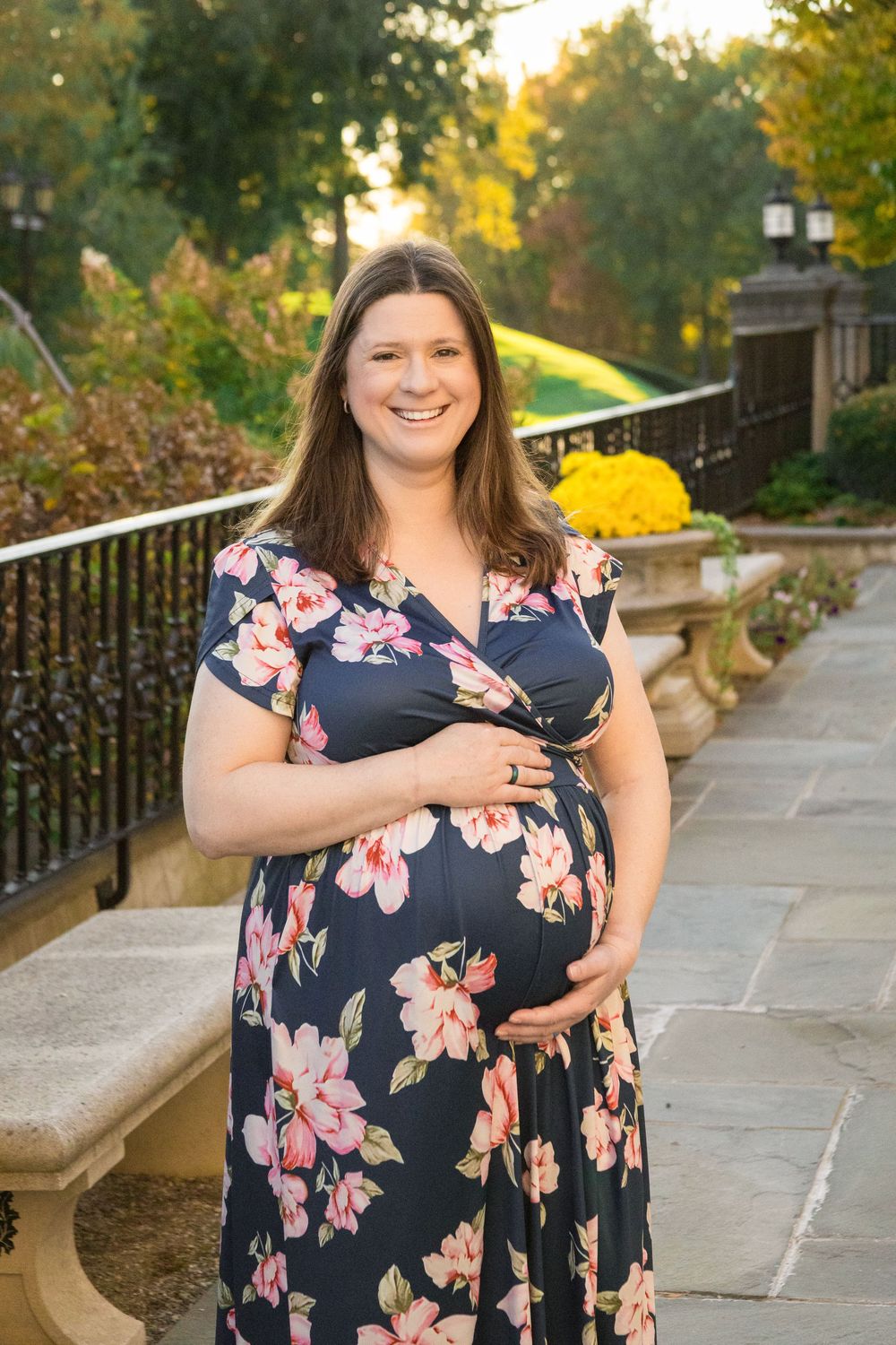 A person in a navy floral dress poses outdoors along a stone walkway during golden hour.