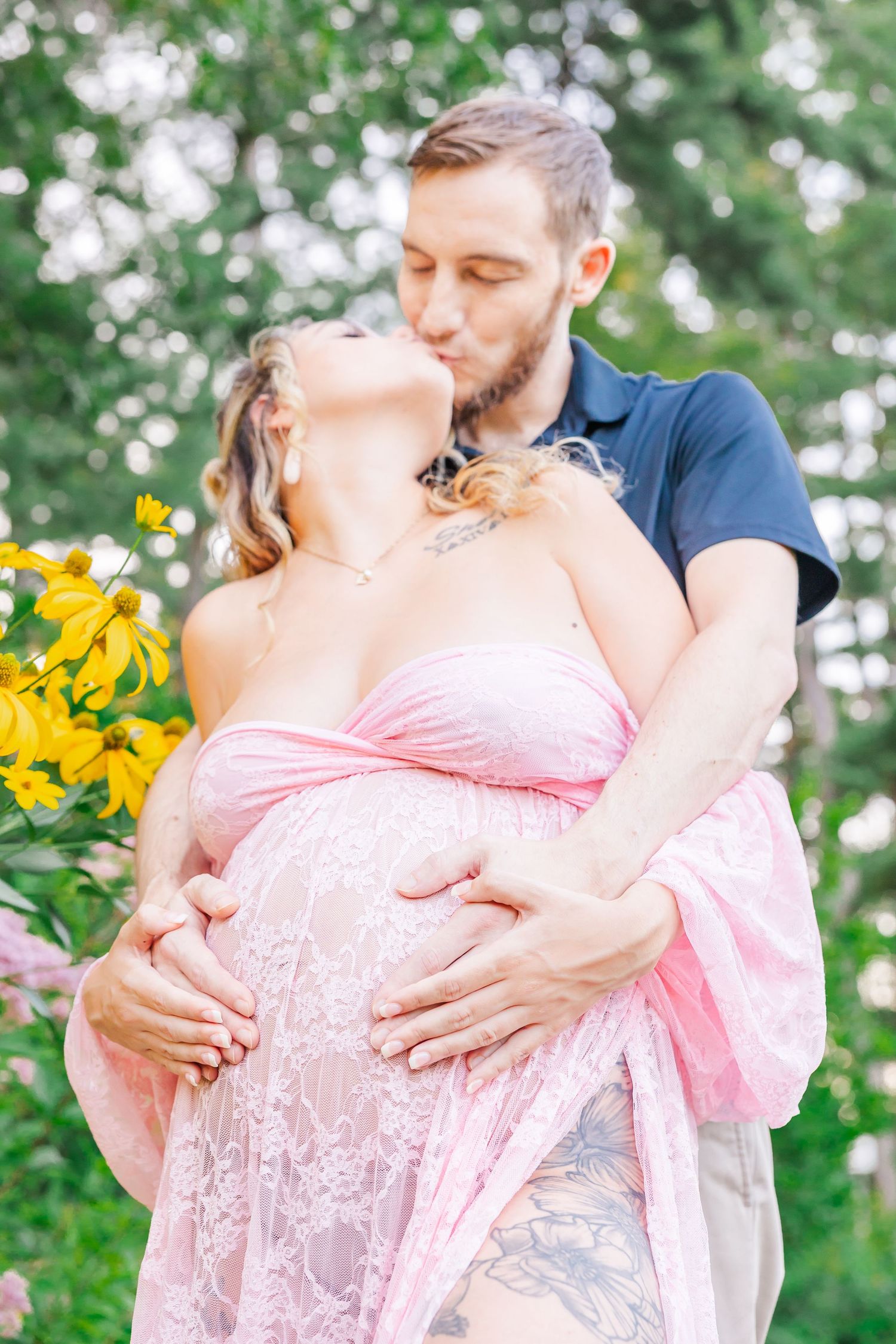 A romantic maternity photo outdoors with the couple embracing near yellow flowers in a garden setting.