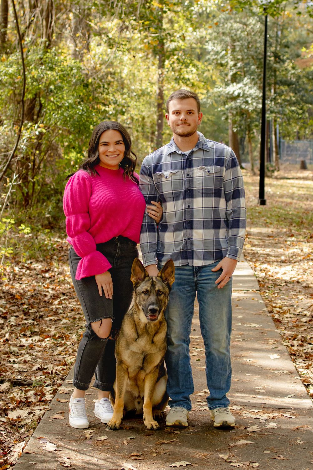 a couple standing with their dog on a path in the park