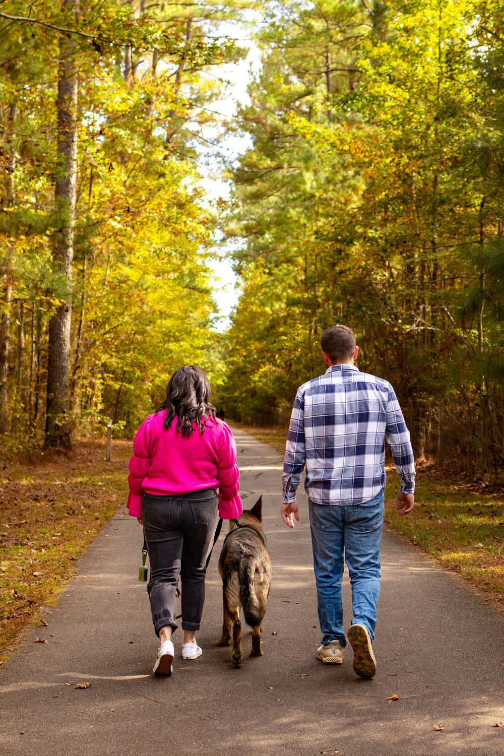 a couple walking away with their dog through a trail in the woods