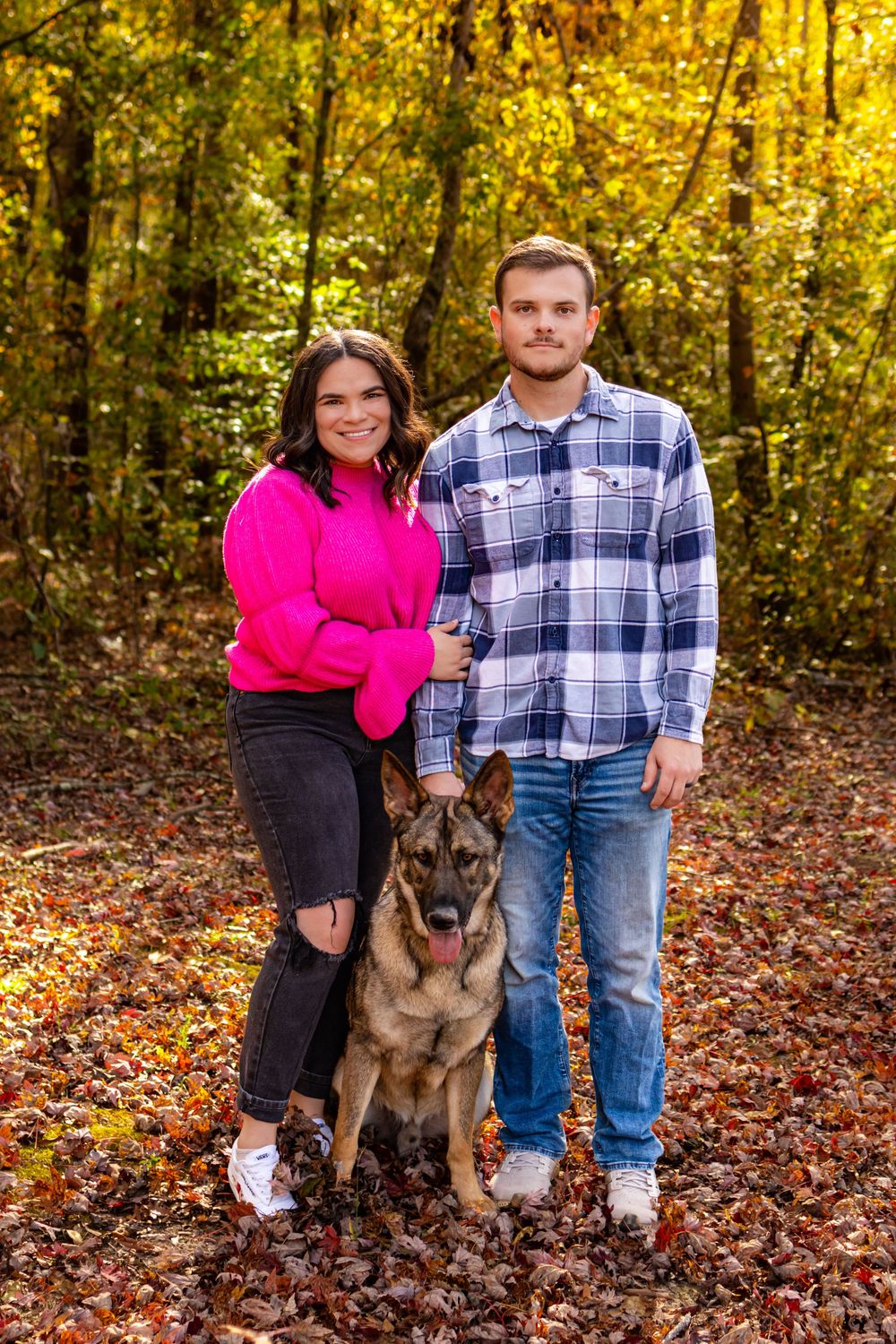 a couple standing in the woods with their dog