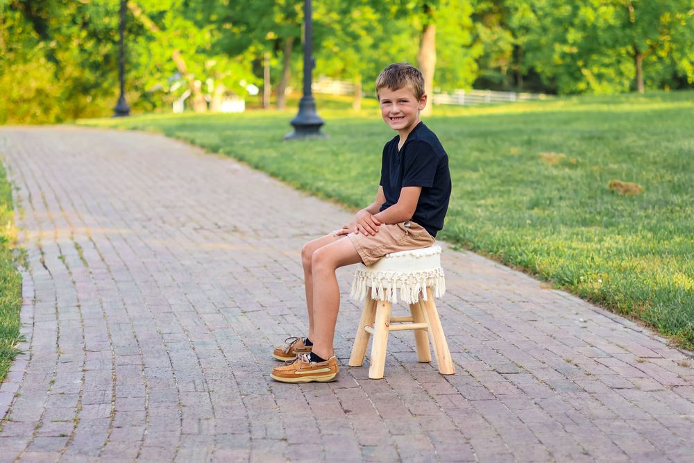 a young child sitting on a stool on a path in a park