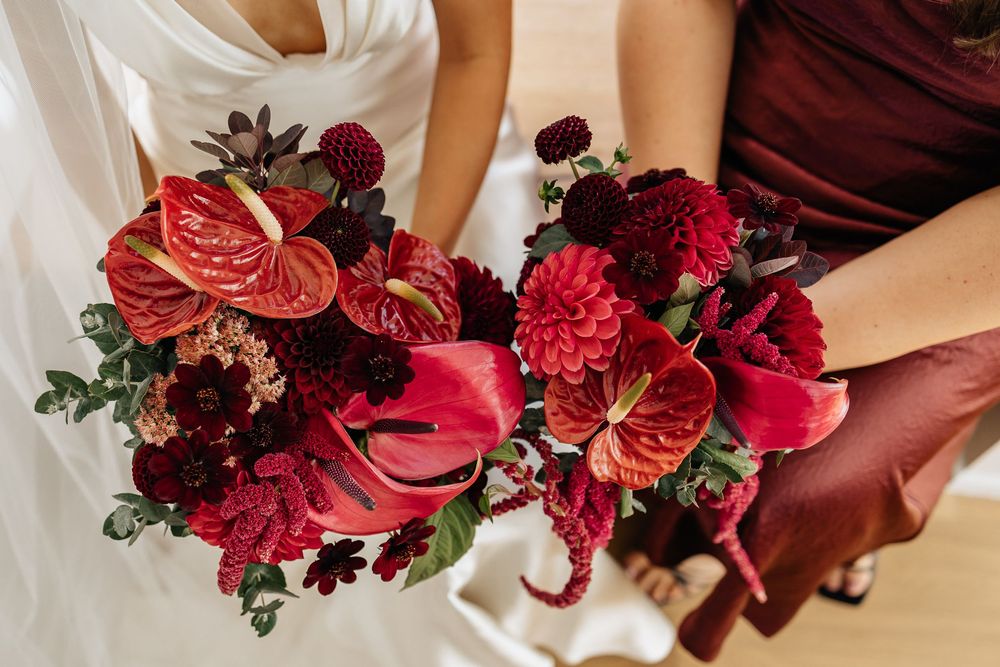 Two wedding bouquets featuring deep red anthurium flowers, burgundy dahlias and rich greenery in a dramatic arrangement.