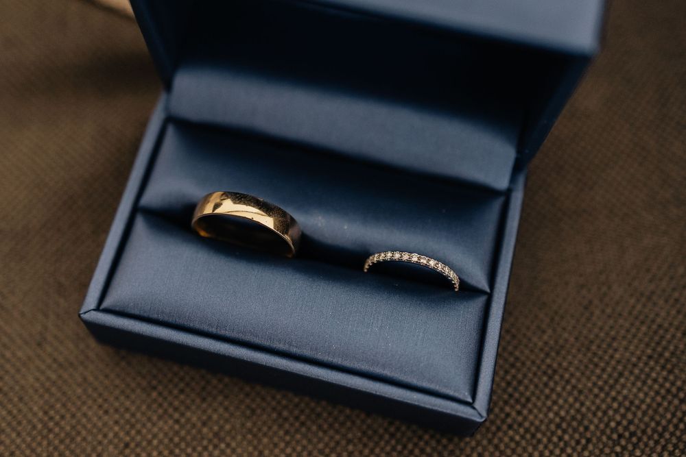 Wedding ring nestled in a navy blue velvet ring box photographed from multiple angles on a textured fabric surface.