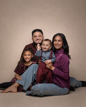 A smiling family of four poses together, wearing burgundy and jeans, including two parents and their young daughter and baby son.