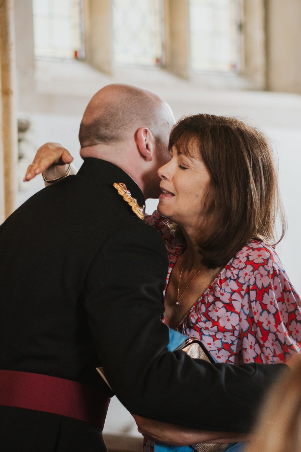 A tender moment shared between a military service member in dress uniform and a woman wearing a red floral dress.